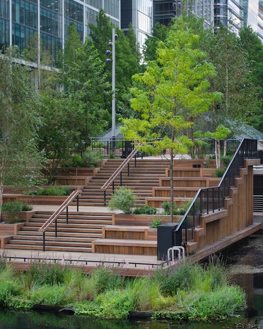 A tranquil riverside garden featuring a modern wooden deck with a set of patio furniture and a large umbrella, overlooking a narrow waterway with calm, dark water reflecting the surrounding greenery. 